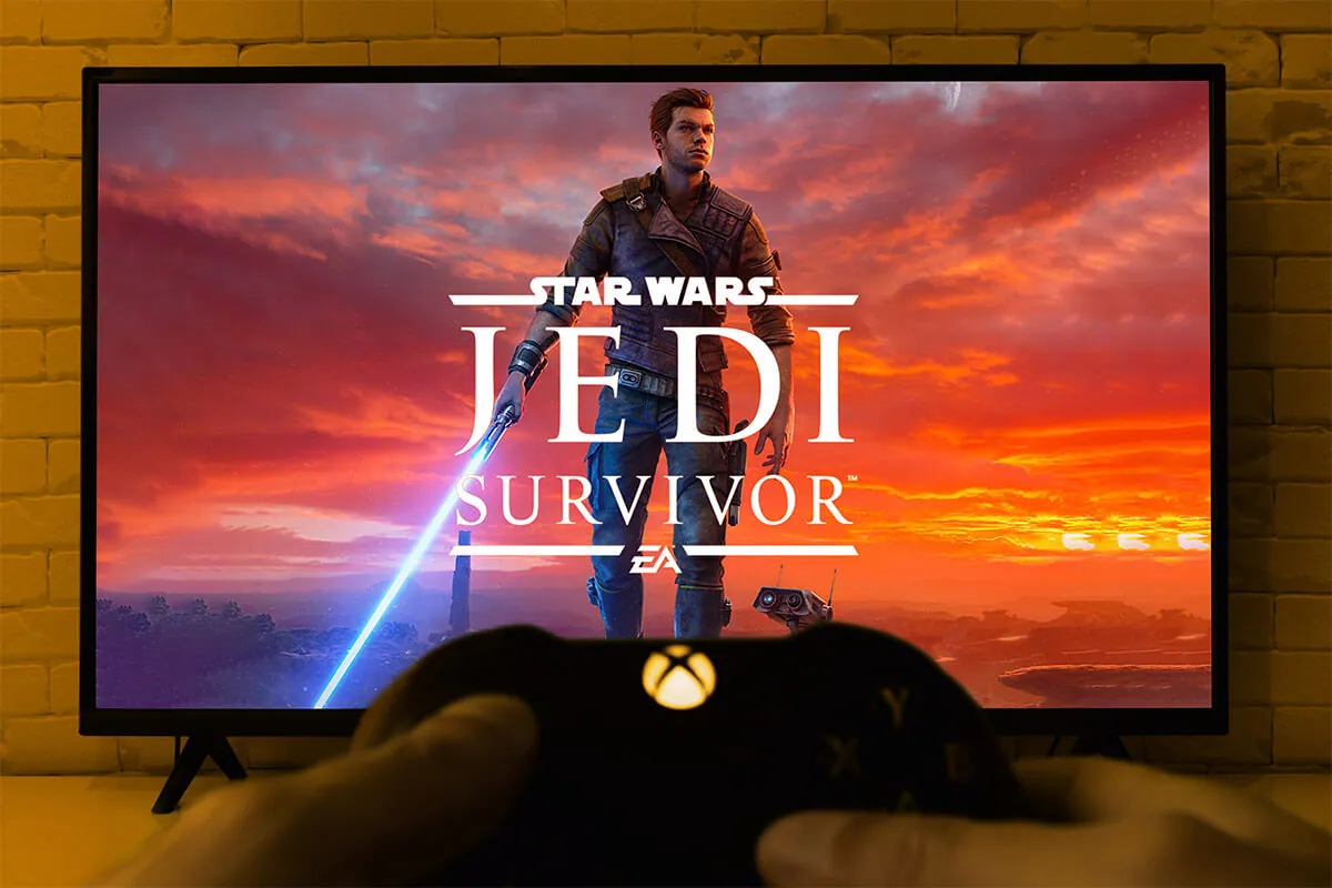 Xbox controller with Star Wars Jedi Survivor logo at TV screen.
