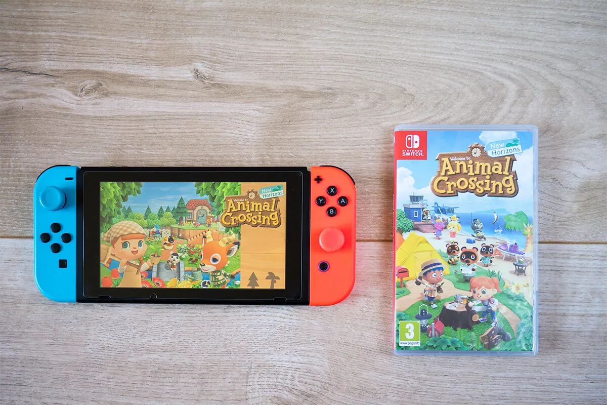 Nintendo switch game console and animal crossing new horizons game on wooden background.