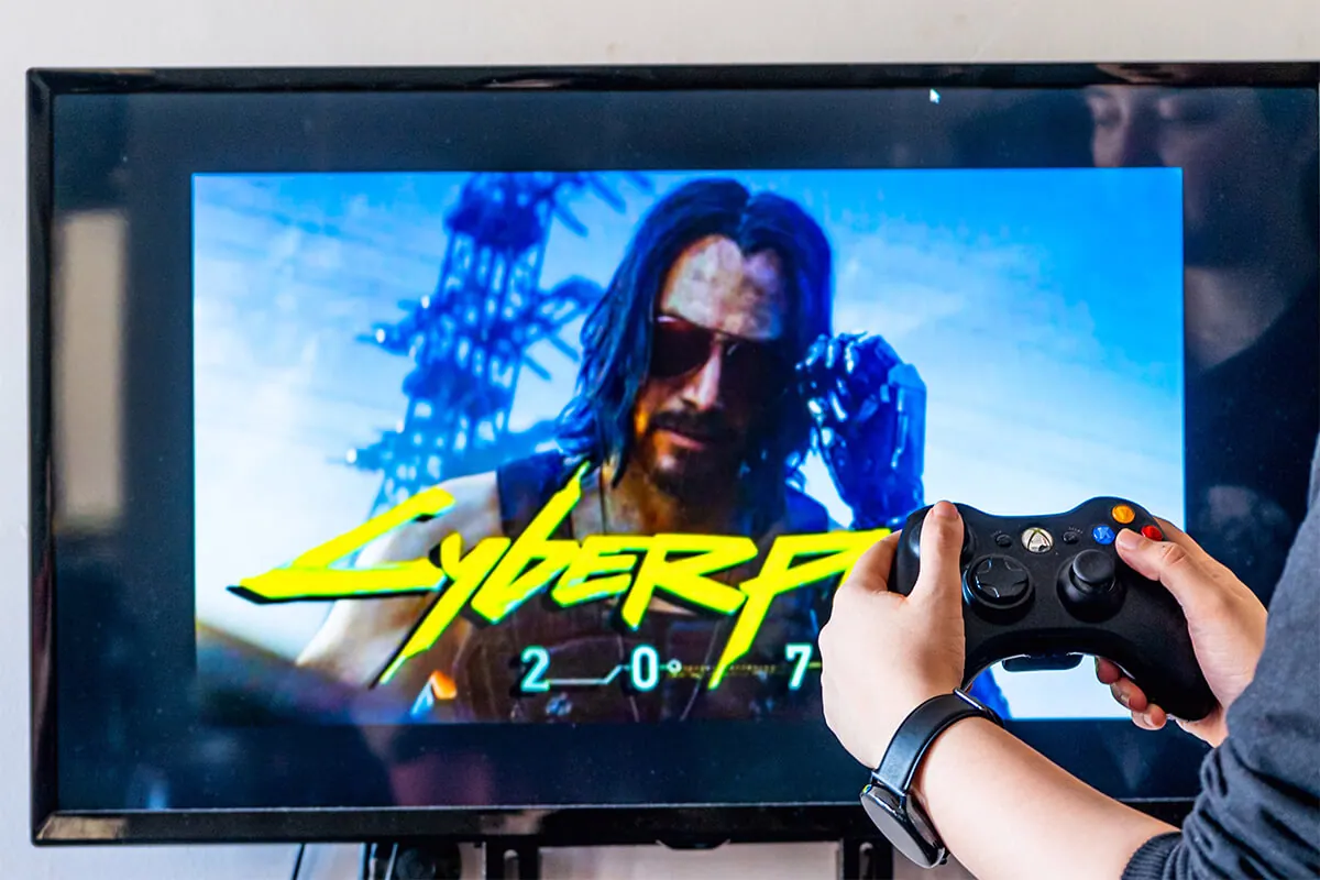 Woman holding a controller and playing Cyberpunk 2077 on a television.
