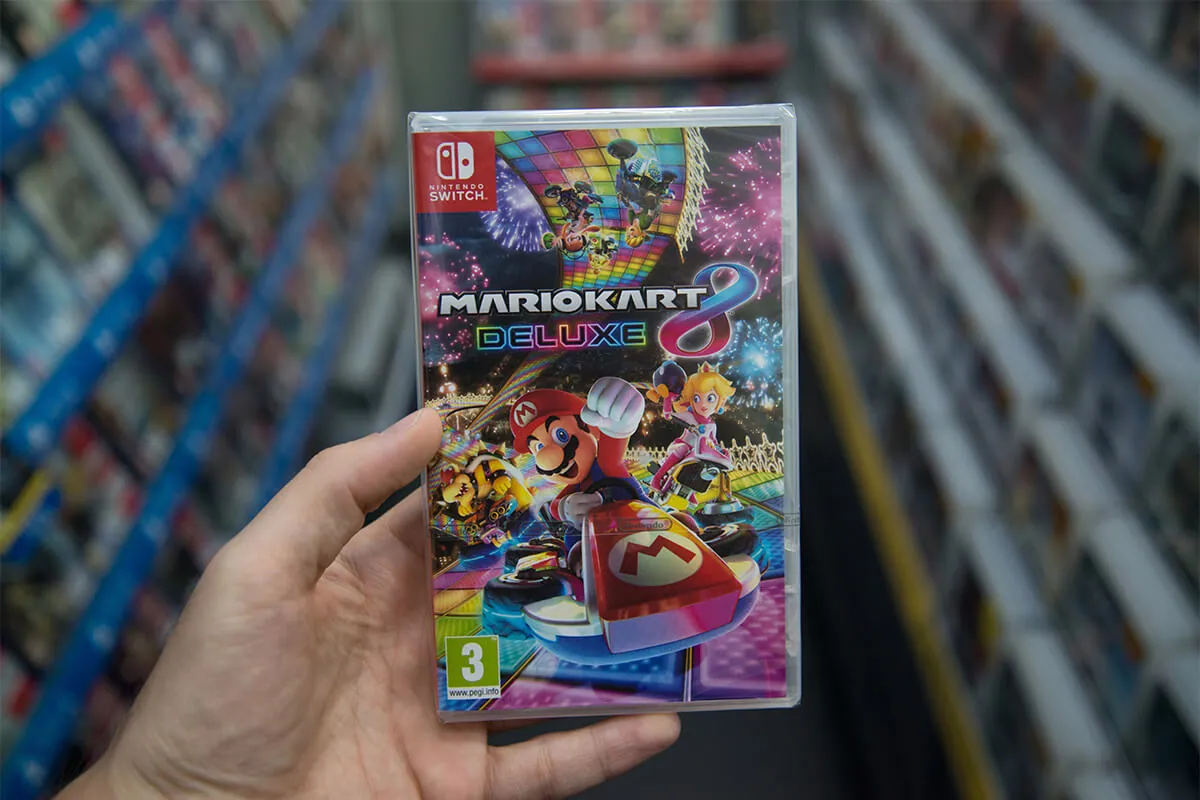 Man holding Mario Kart 8 Deluxe videogame on Nintendo Switch console in store.