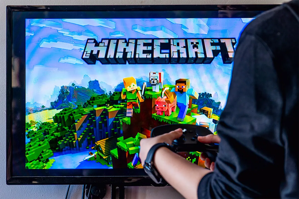 Woman holding a steam controller and playing popular video game Minecraft on a television and PC.