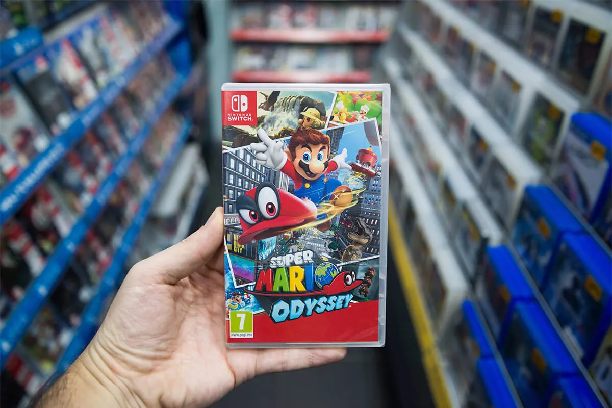 Man holding Super Mario Odyssey videogame on Nintendo Switch console in store.